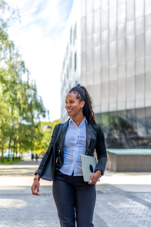 Vertical photo with copy space of a latin beauty businesswoman walking distracted with laptop and handbag along the cityの写真素材