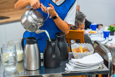 Unrecognizable nurse preparing breakfast pouring milk and coffee on jars in a trolley in a geriatricsの写真素材