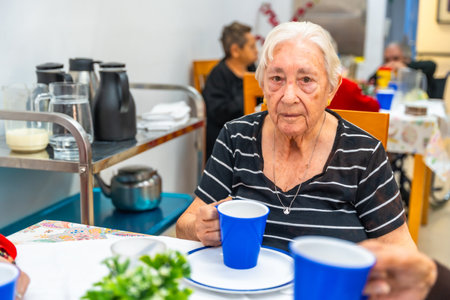 Portrait of a senior woman drinking morning coffee sitting on shared table at dining room at geratricsの写真素材