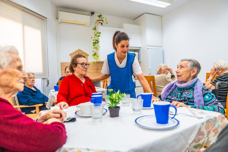 Female caucasian caregiver and senior people in the dining hall of a nursing homeの写真素材