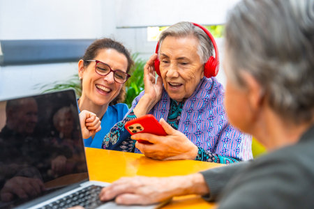 Senior woman assisted by caregiver having fun listening to music with mobile phone at geriatricsの写真素材