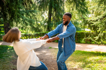 Multiracial couple holding hands and dancing in circles in a parkの写真素材