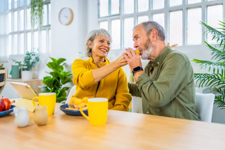 Senior woman feeding her husband in a romantic gesture in the morning sharing breakfast at homeの写真素材