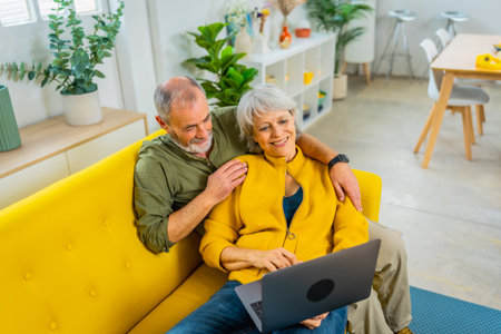 Elevated view photo of a casual senior couple lying on the sofa relaxing using laptopの写真素材
