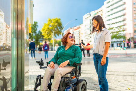 Disabled woman in wheelchair and caregiver waiting at metro elevator in the city during sunny dayの写真素材