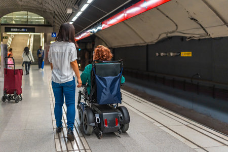 Rear view of a disabled caucasian adult woman in wheelchair and asian friend walking along metro stationの写真素材