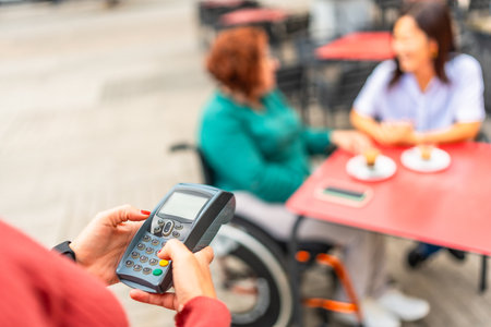 Waiter preparing the terminal to charge a woman with a disability and her friend for some coffeesの写真素材