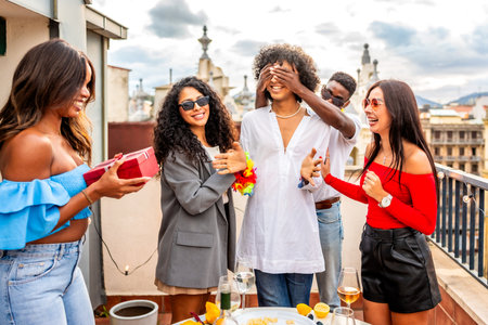 Multiracial group of friends covering eyes of a man giving her a present at a rooftop partyの写真素材