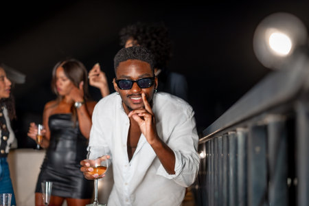 Latin cool man gesturing while dancing and drinking alcohol during roof party at nightの写真素材