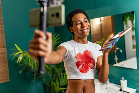 Happy latin man using mobile phone while recording makeup tutorial