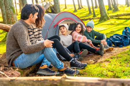 Parents talking with their three children sitting on camping tent enjoying a weekend trekking togetherの写真素材