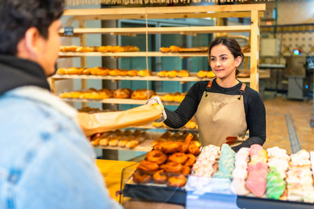 Latin young man buying artisan bread in a modern bakery attended by a friendly latin young woman