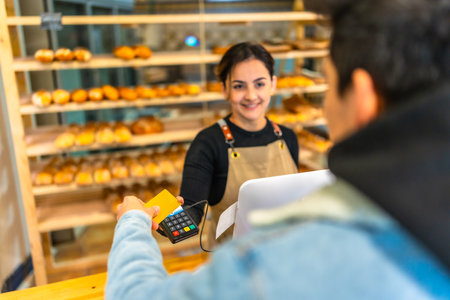 View over shoulder of a young man paying using credit card in a bakery shopの写真素材
