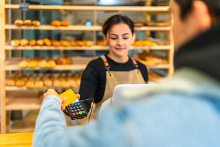 Rear view of a latin man paying with credit card and contact less terminal in an artisan bakeryの写真素材
