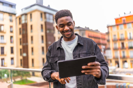 Happy african man touching the screen of a digital tablet and smiling outdoors in the city