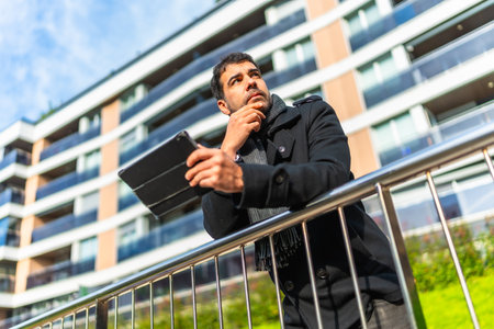Low angle view portrait of a caucasian pensive businessman in casual winter clothes using digital tablet standing in the cityの写真素材