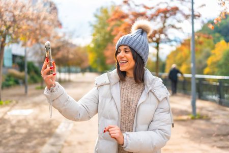 Woman wearing warm clothes and woolly hat smiling while talking during video call with mobile phone...