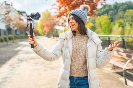 Young beauty female vlogger wearing warm winter clothes recording video in the city park