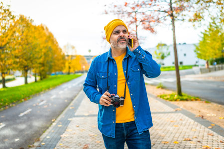 Male mature tourist talking to the mobile while walking along a street visiting a city