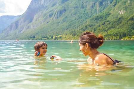 Mother and son enjoying summer fun, playing with toys while swimming in the refreshing waters of lake Bohinj, surrounded by the Julian Alpsの写真素材