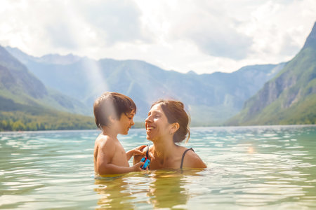 Mother and son enjoying summer holidays, playing in the refreshing water of lake Bohinj, surrounded by the stunning Julian Alpsの写真素材
