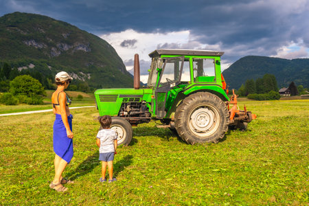 Woman and her son are observing a green tractor in a field near lake Bohinj, Slovenia, during their summer vacationの写真素材