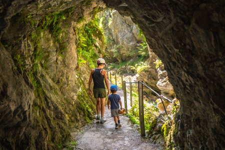 Mother and son walking through a narrow passage carved into the rock face at Tolmin Gorge in Slovenia, enjoying a summer day exploring natureの写真素材