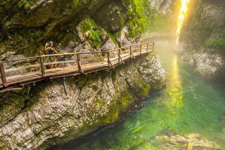 Tourists enjoying a scenic walk along the wooden pathway above the emerald radovna river, surrounded by the steep cliffs of vintgar gorgeの写真素材