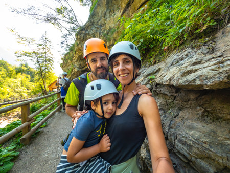 Family wearing helmets taking selfie while hiking on wooden walkway next to rock wall in beautiful Vintgar Gorge near Bled, Sloveniaの写真素材