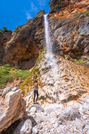 Female hiker with open arms enjoying the view of Rinka waterfall in Logarska Dolina, Kamniksavinja Alps, Slovenia, during summerの写真素材