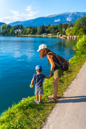 Mother and son holding hands, enjoying the scenic view of lake bled, with the julian alps in the background, during their summer vacationの写真素材