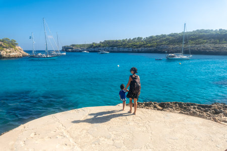 Mother and son enjoying a sunny day at Cala S'Amarador beach in Mallorca, Spain, admiring the...