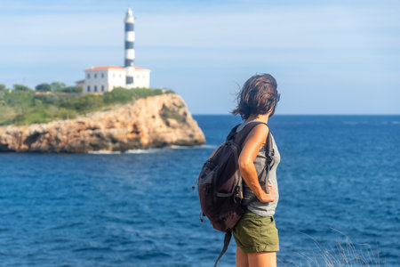 Female tourist with backpack contemplating the scenic Portocolom lighthouse on a sunny day in Mallorca, Balearic Islandsの写真素材