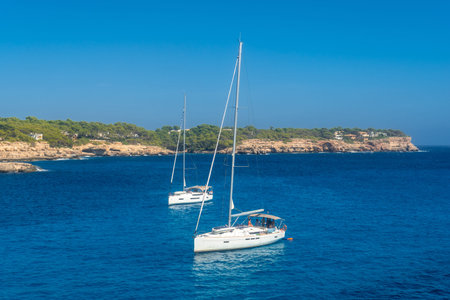 Two sailboats anchoring in the turquoise waters of Cala Mondrago, enjoying sunny summer weather and...