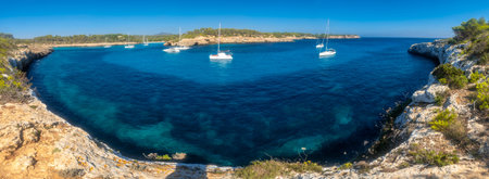 White sailboats are anchored in the turquoise waters of Cala Mondrago, a beautiful bay in Mallorca,...