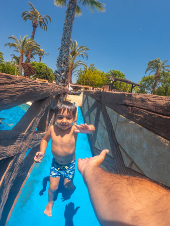 Happy child enjoying a waterslide and reaching for parent's hand at a water park, summer vacation funの写真素材