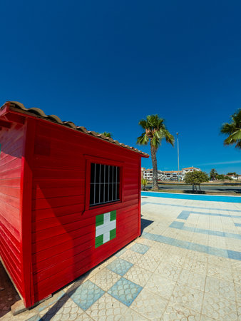 Red wooden lifeguard station with accessibility features for disabled people, located on a sunny beach with palm trees and clear blue skyの写真素材