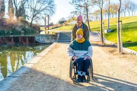 Two male friends enjoying a sunny day at the park, one pushing the wheelchair of his disabled friend