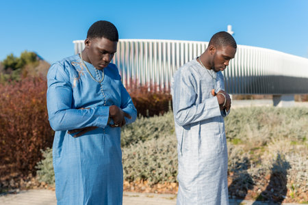 Two young African Muslim men wearing traditional clothing are praying outdoors, expressing their devotion and spiritualityの写真素材