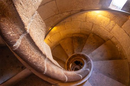 Warm light illuminating ancient stone spiral staircase descending into the depths of Barcelona cathedral, a captivating architectural marvelの写真素材