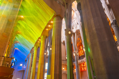 Sunlight illuminates colorful stained glass windows, casting vibrant hues onto architectural columns inside Sagrada Familia in Barcelonaの写真素材