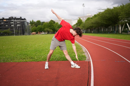 Full length photo of a man standing warming up and stretching before running on a track