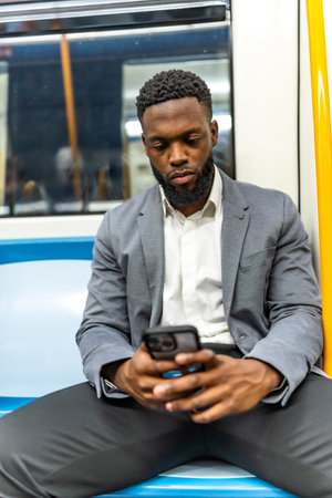 Young businessman sitting in a subway train, using a smartphone for browsing, checking emails, and staying connected while commutingの写真素材