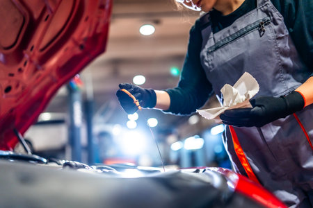Professional female mechanic inspecting engine oil level with dipstick and rag in a car repair shopの写真素材