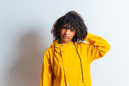 Studio portrait of a young woman wearing a yellow raincoat and scratching her head against a white backgroundの写真素材