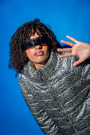Stylish model showcasing futuristic eyewear and a trendy animal print jacket against a vibrant blue...