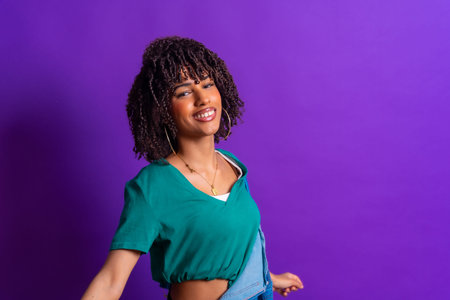 Carefree young latin woman with curly hair dancing, wearing a green t shirt and denim jacket on a...