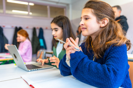 Smart young female students thinking and learning using laptop computer and notebook in elementary school classroomの写真素材