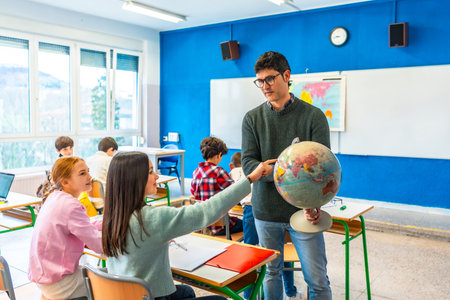 Geography teacher engaging students by pointing out countries on a globe during an interactive lesson in a lively classroom settingの写真素材