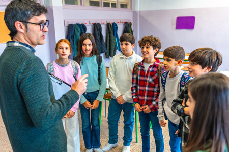 Male teacher holding clipboard explaining lesson to group of elementary school students in classroomの写真素材